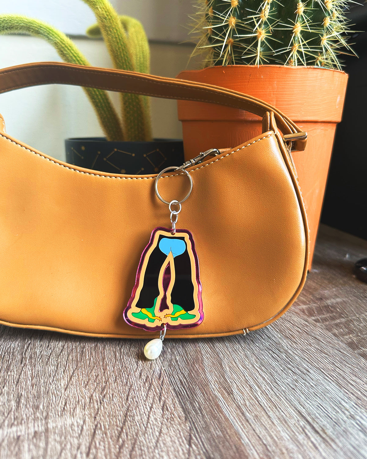 Brown handbag with a colorful bag charm keychain featuring a chaps design on a wooden surface.